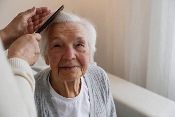 Unrecognizable female expressing care towards an elderly lady, brushing her hair with a comb. Granddaughter helping granny with a haircut. Family values concept. lose up, copy space, background.